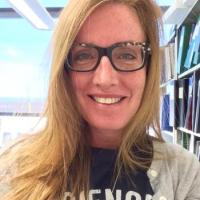 A woman wearing a shirt that says "science" stands in front of a bookshelf